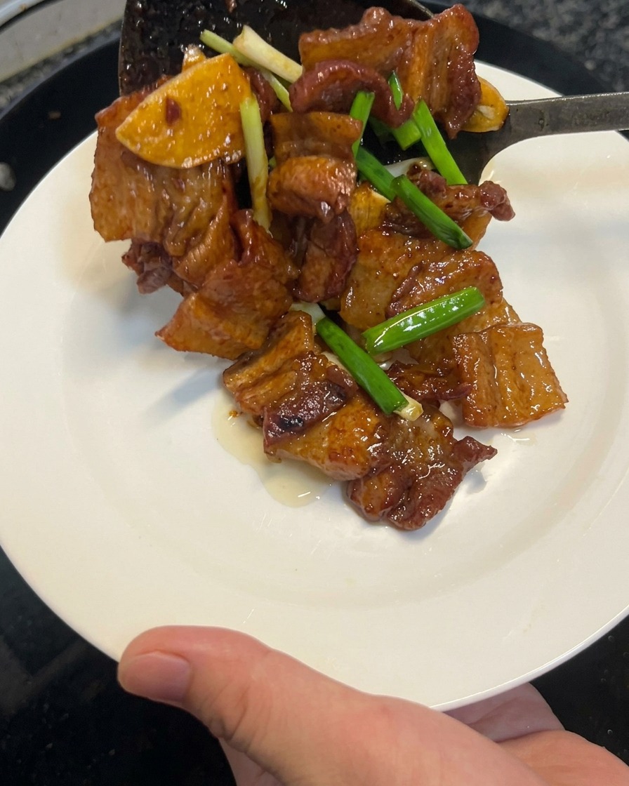 Panza de cerdo cocida a la salsa de soja siendo retirada de un wok con una espátula a un plato blanco limpio.