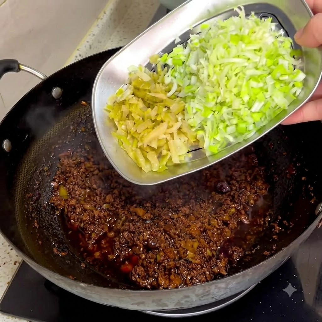Mostaza encurtida picada y cebollas verdes siendo deslizadas desde una bandeja de metal hacia una salsa de carne oscura en un wok.