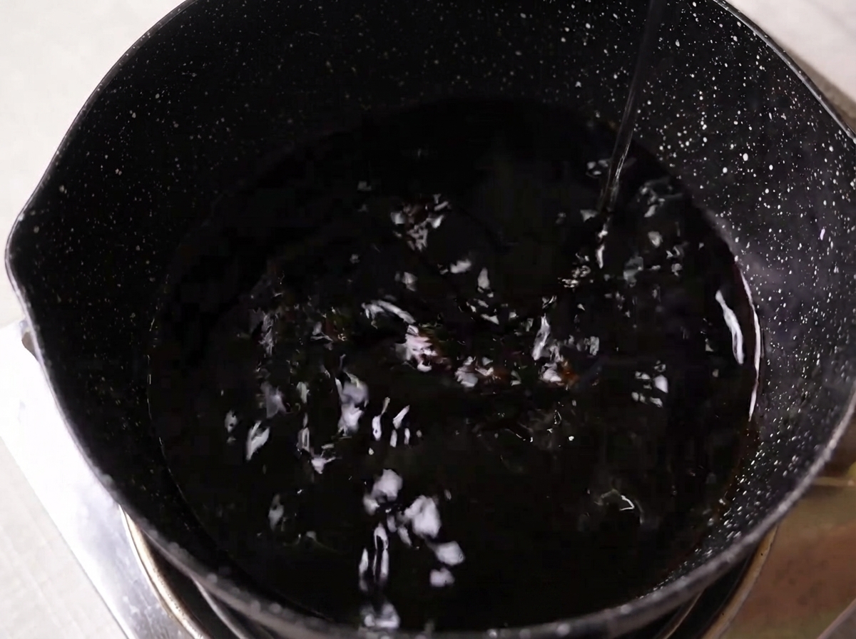 Salsa de soja, mirin, sake y azúcar blanca mezclándose en una olla oscura sobre una estufa.