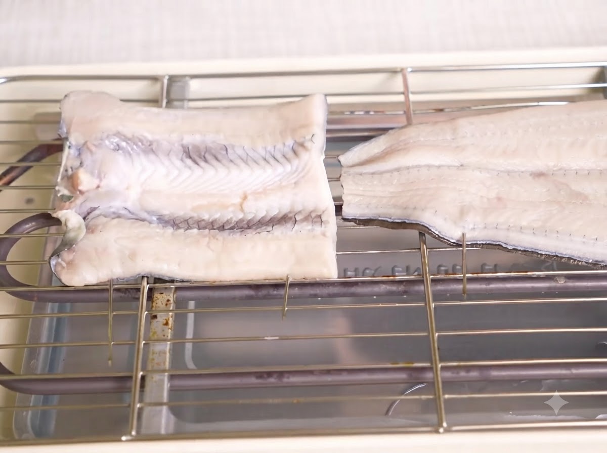 Dos piezas de anguila cruda en mariposa y ensartada colocadas en una rejilla metálica sobre una parrilla eléctrica.