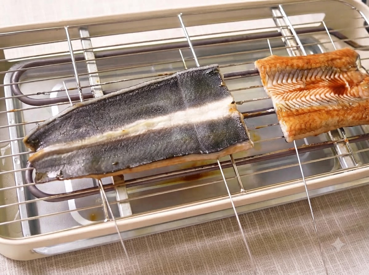 Filetes de anguila cocinándose en una parrilla eléctrica con brochetas de metal atravesando la carne.