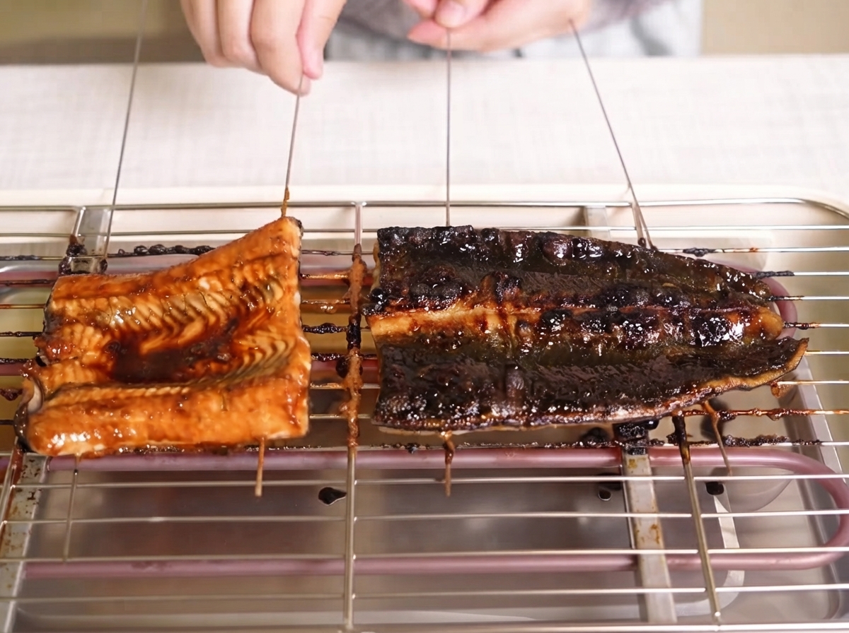 Filetes de anguila dorándose mientras se les cepilla con una salsa oscura brillante en una rejilla de parrilla.