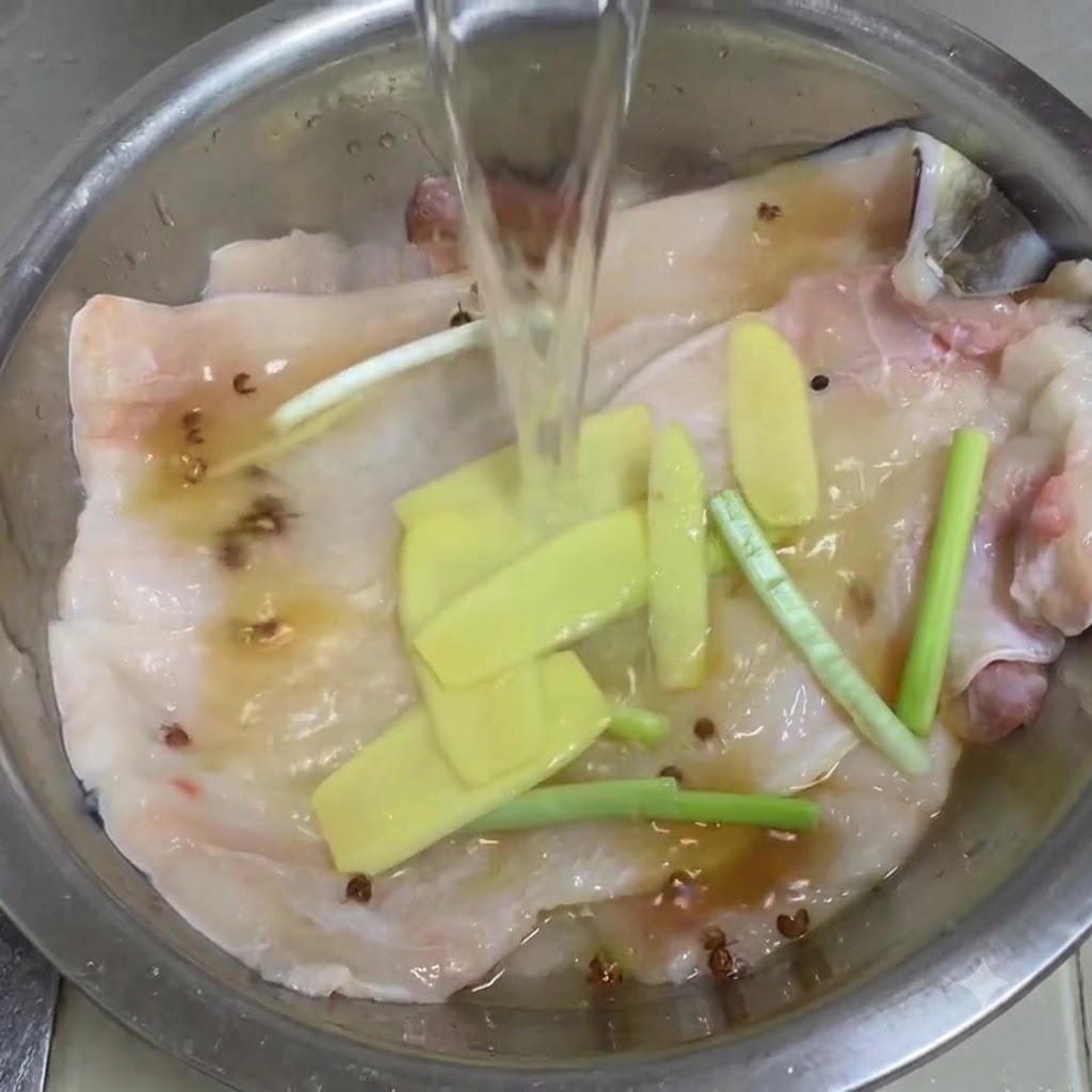 Agua cristalina vertiéndose en un tazón de metal con filetes de anguila, jengibre, cebollines y granos de pimienta de Sichuan.