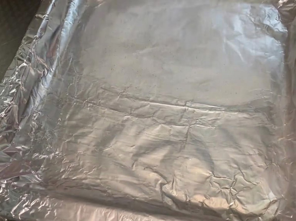 Una bandeja de metal para hornear cubierta con papel aluminio arrugado y untada con una capa brillante de aceite de cocina.