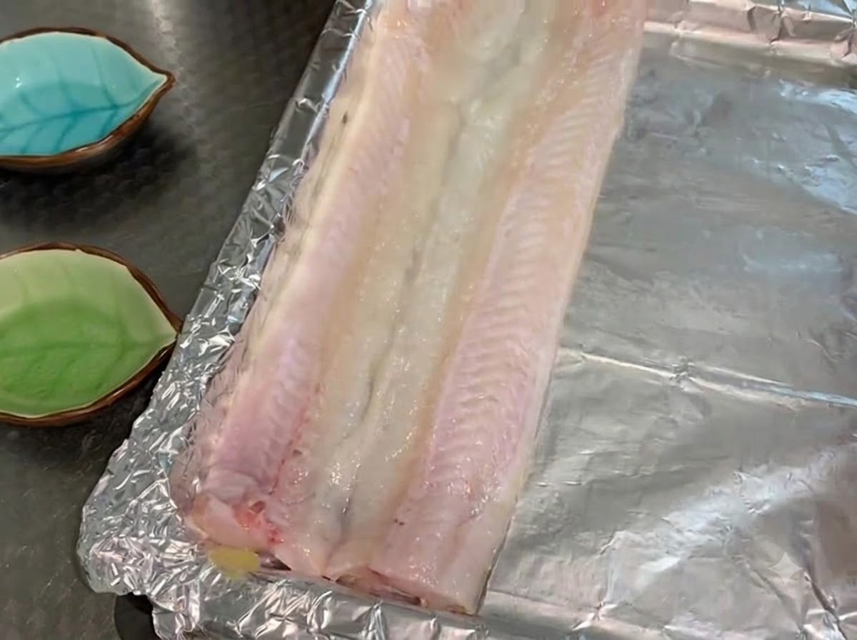 Filetes de anguila cruda colocados en una sola capa sobre una bandeja de horno forrada con aluminio y untada con aceite.