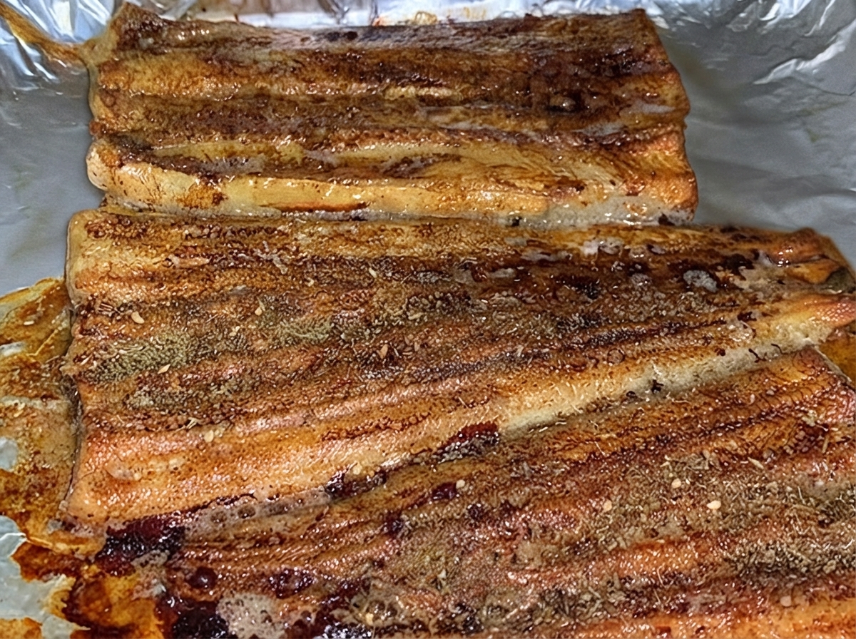 Filetes de anguila horneados y espolvoreados uniformemente con una capa de polvo sazonador BBQ marrón dentro de una sartén de horno.
