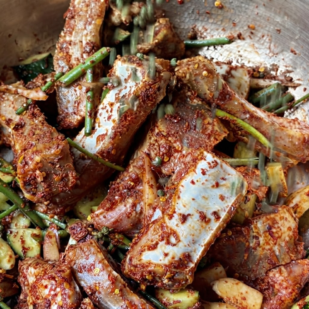 Un puñado de granos enteros de pimienta de Sichuan verde cayendo sobre las costillas de cerdo marinadas.