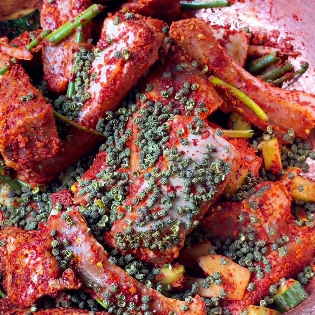 Una vista de cerca de los granos enteros de pimienta de Sichuan roja esparcidos sobre los trozos de carne roja sazonada.