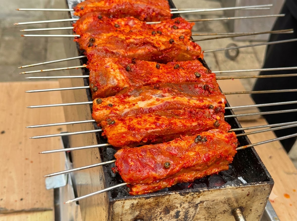 Múltiples brochetas de costillas con revestimiento rojo alineadas y asándose sobre un foso de carbón.