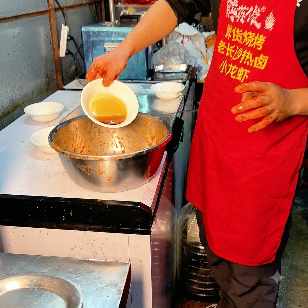 Aceite de cocina siendo vertido desde un tazón pequeño hacia las costillas de cerdo sazonadas.