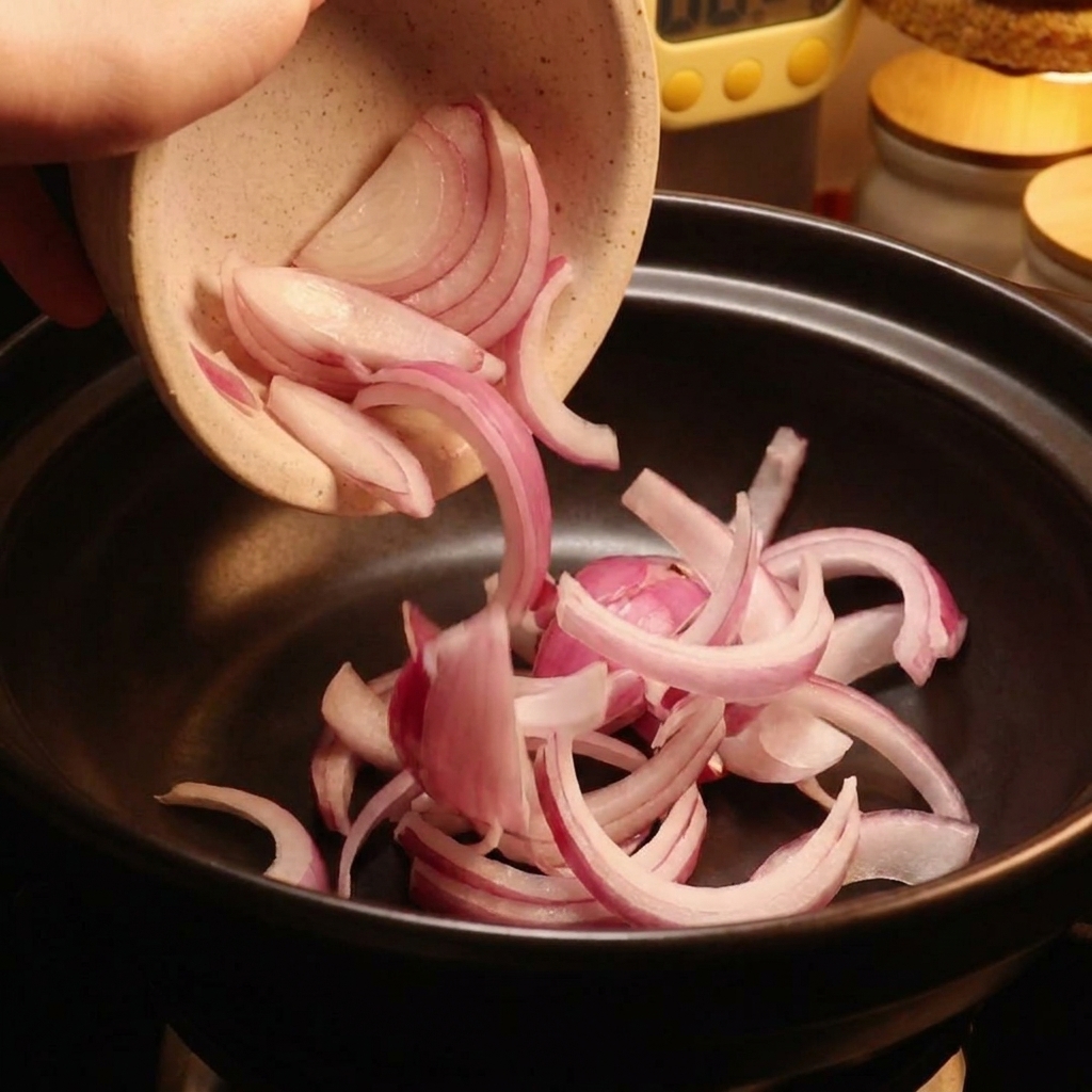 Rodajas de cebolla roja siendo vertidas desde un tazón de cerámica en una olla negra.