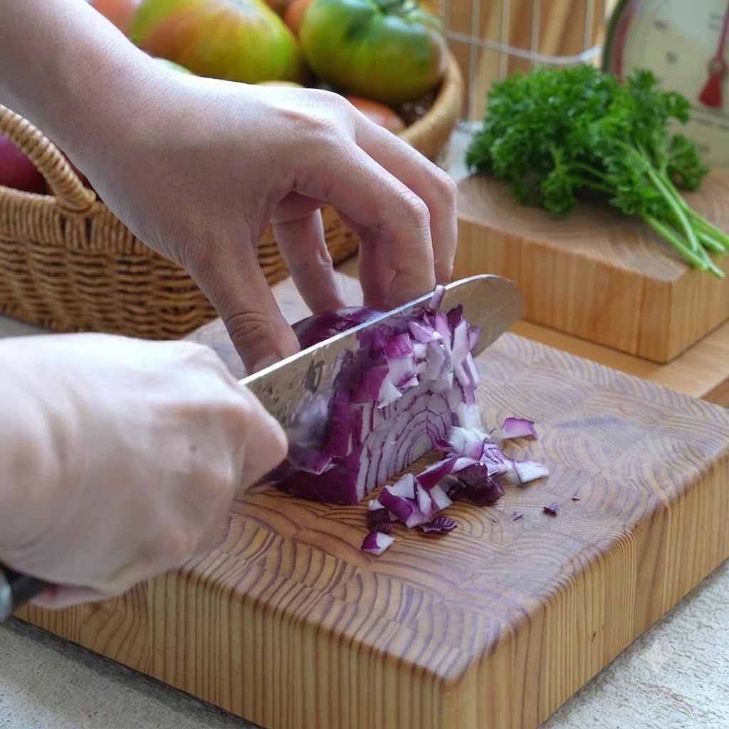 Cebolla morada cortada en cubitos pequeños con un cuchillo sobre una tabla de madera.