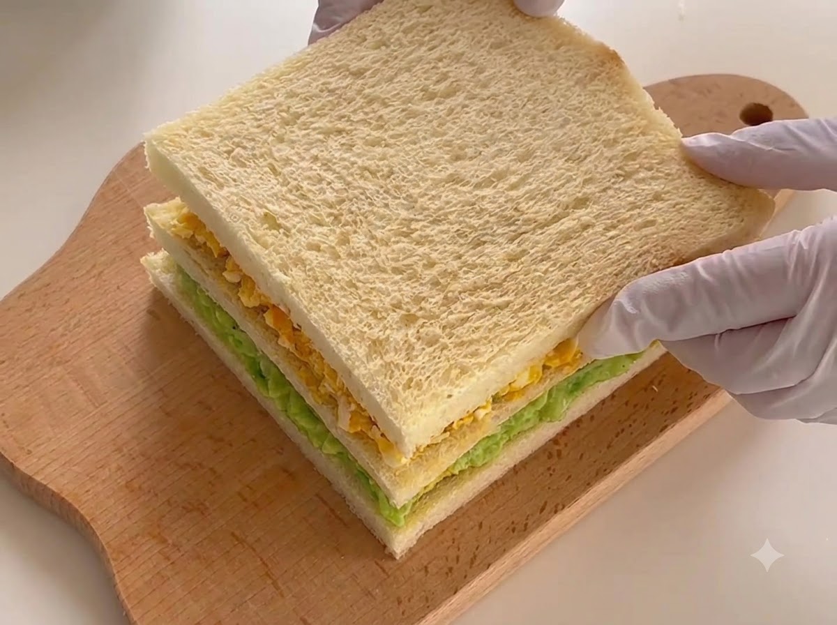El sándwich de tres capas completamente ensamblado descansando en una tabla de cortar, listo para cortar.