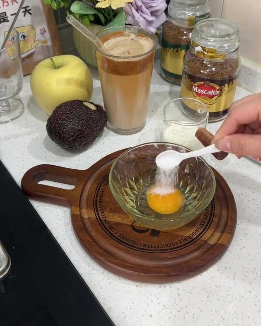 Una pequeña cuchara blanca añadiendo sal directamente sobre la yema de un huevo crudo en un tazón de vidrio.