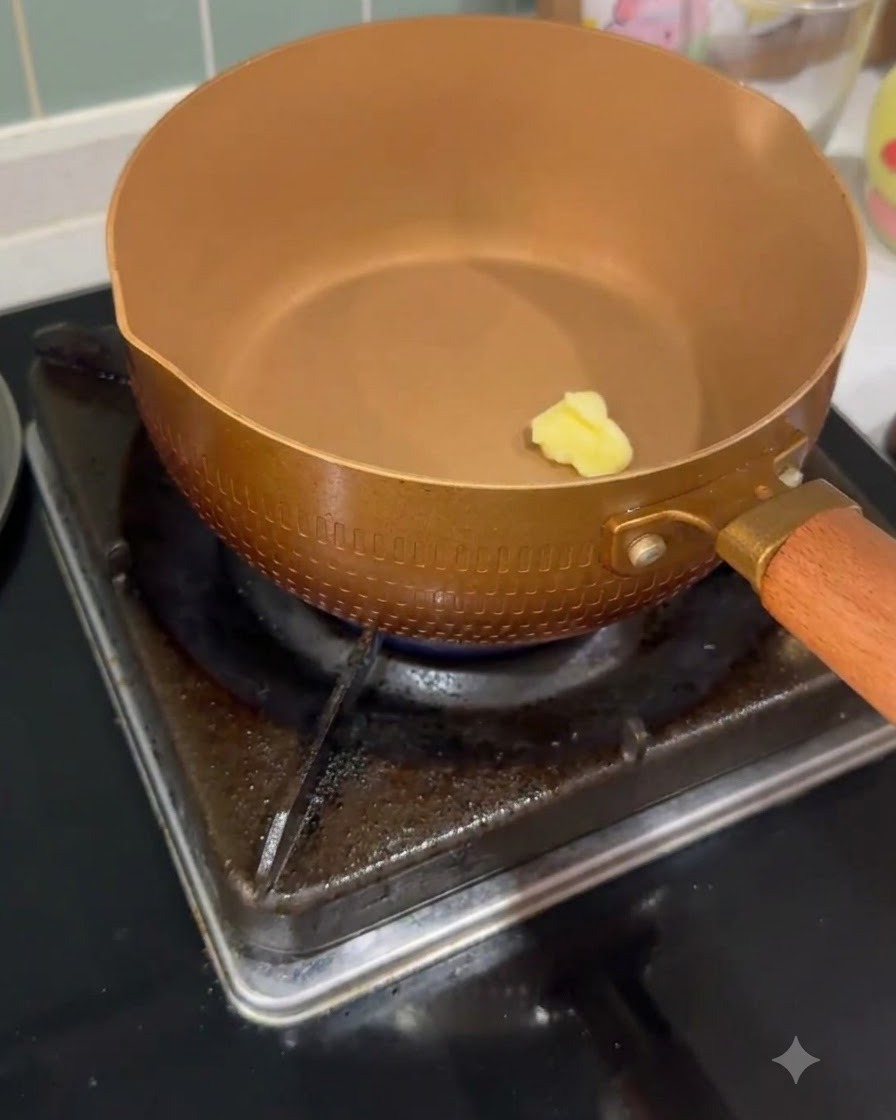 Un pequeño trozo de mantequilla derritiéndose dentro de una sartén calentada de color cobre en una hornilla de gas.