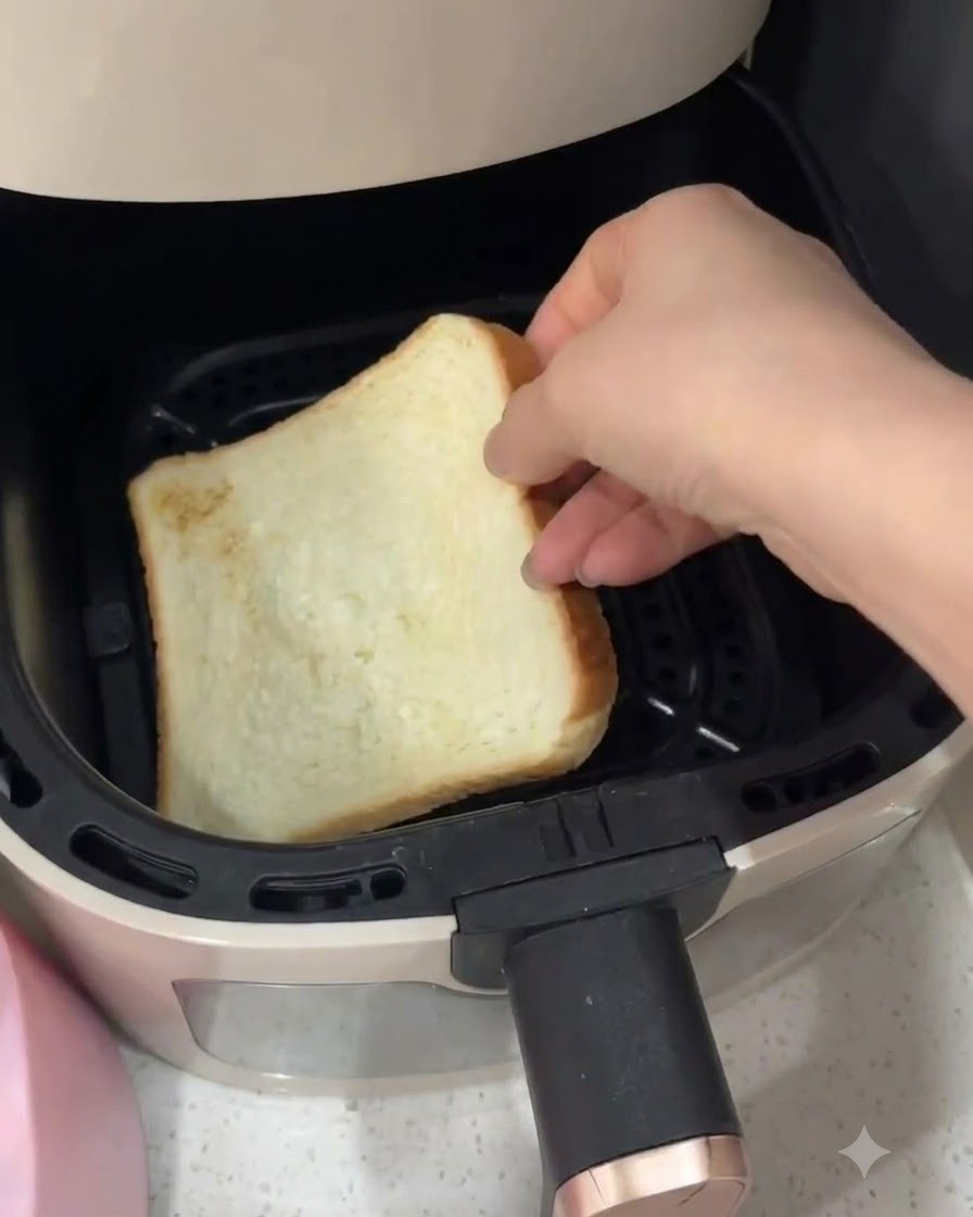 Una mano colocando una rebanada de pan blanco de molde dentro de una cesta de freidora de aire.