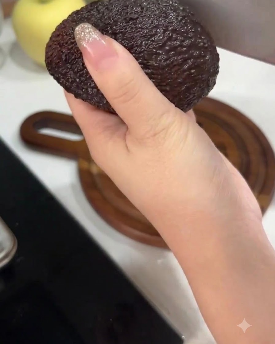 Una mano sosteniendo un aguacate mientras lo corta por la mitad con un cuchillo de cocina grande.