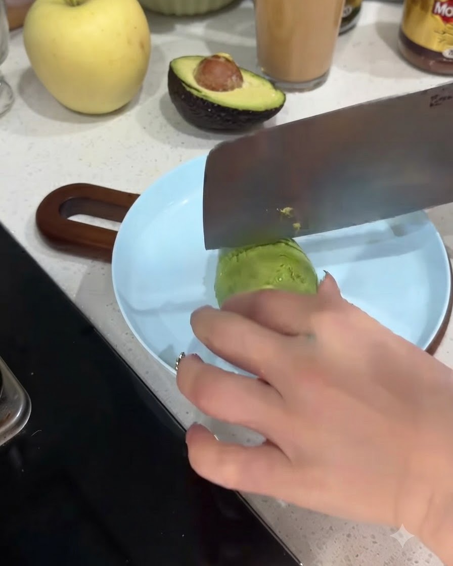 Una mitad de aguacate siendo cortada en rodajas finas sobre un plato azul claro.