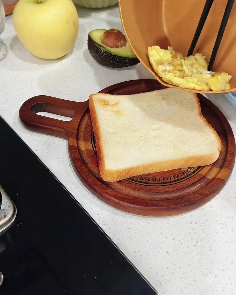 Huevos revueltos cocinados siendo transferidos desde una sartén de cobre a una rebanada de pan blanco tostado sobre una tabla de madera.