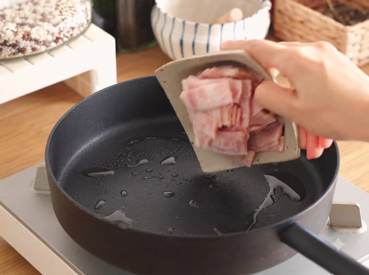Tiras de tocino chisporroteando en una sartén con una pequeña cantidad de aceite.