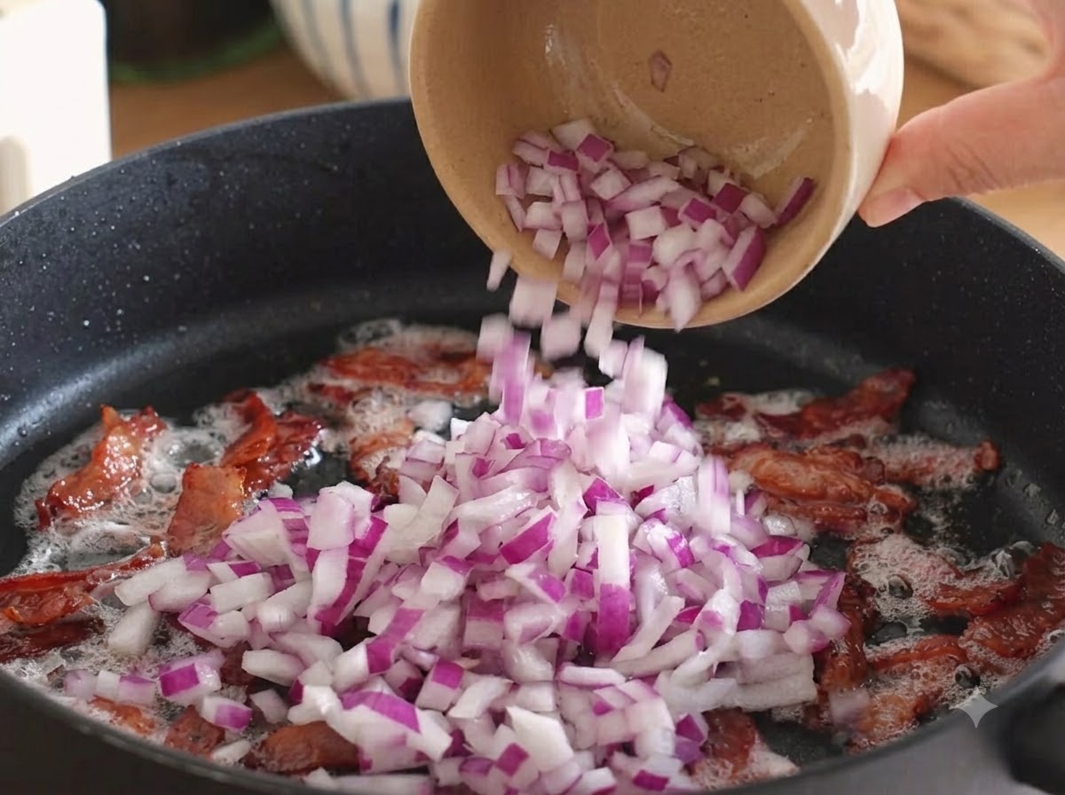Cebollas moradas picadas siendo vertidas en la sartén sobre el tocino cocido.