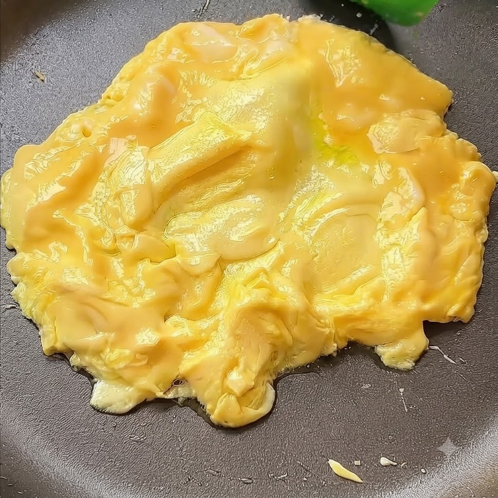 Huevos siendo empujados hacia el centro de una sartén con una espátula.