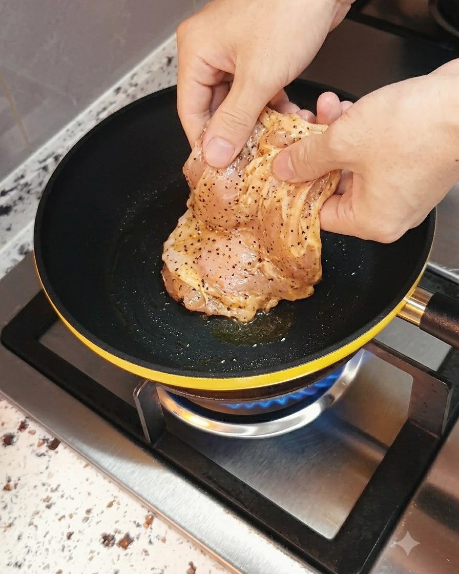 Pechuga de pollo marinada siendo colocada en una sartén caliente con una llama de gas debajo.