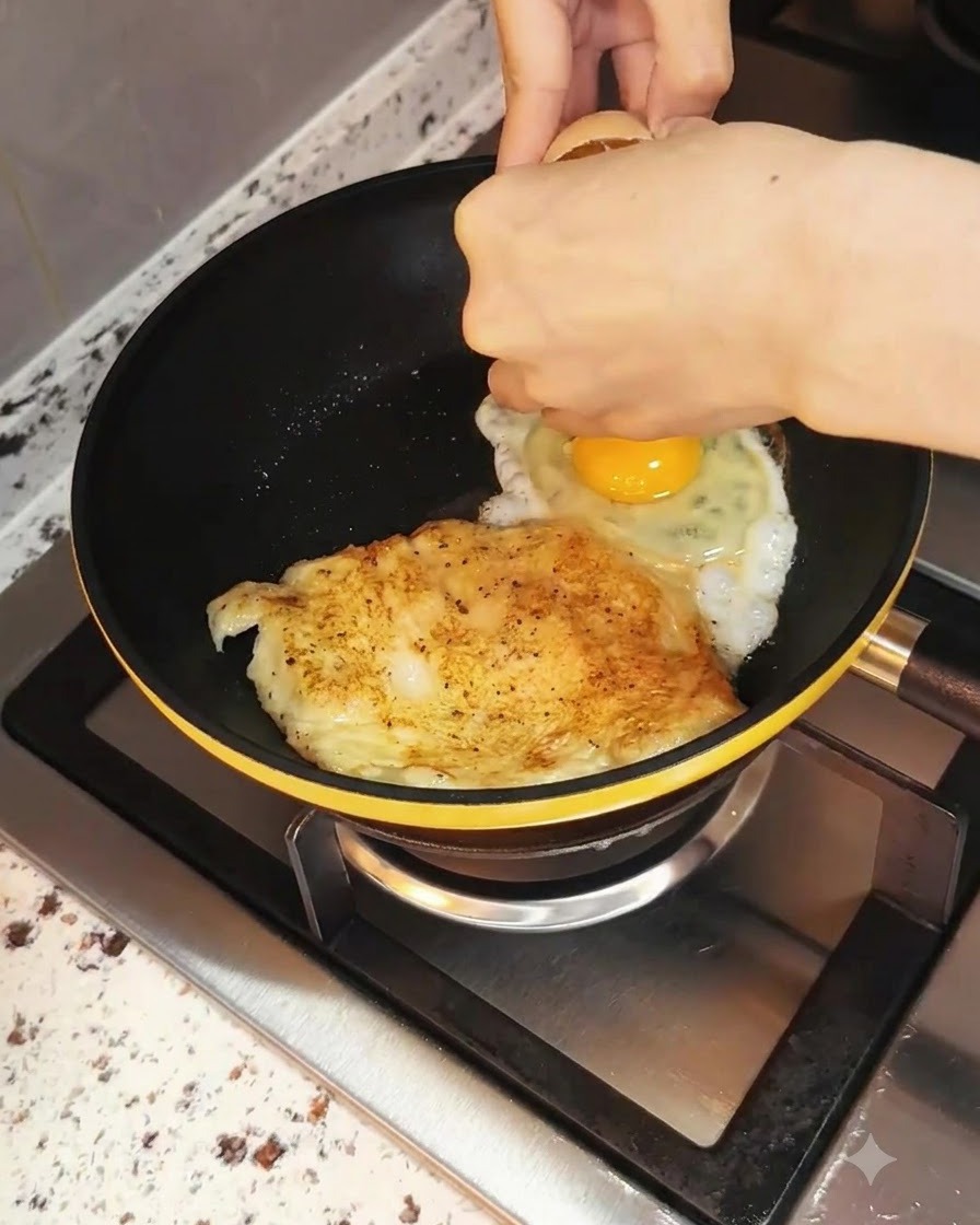 Un huevo siendo cascado en la sartén al lado del pollo que se está cocinando.