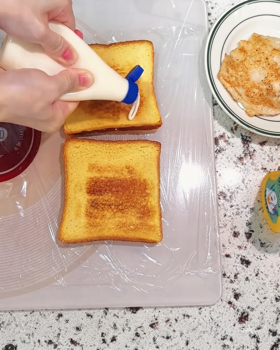 Mayonesa siendo exprimida de una botella sobre rebanadas de pan tostado en una tabla de cortar.