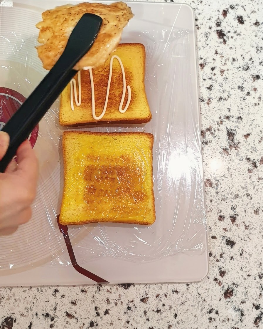 Pechuga de pollo cocida siendo transferida con pinzas sobre una rebanada de pan tostado con salsa.