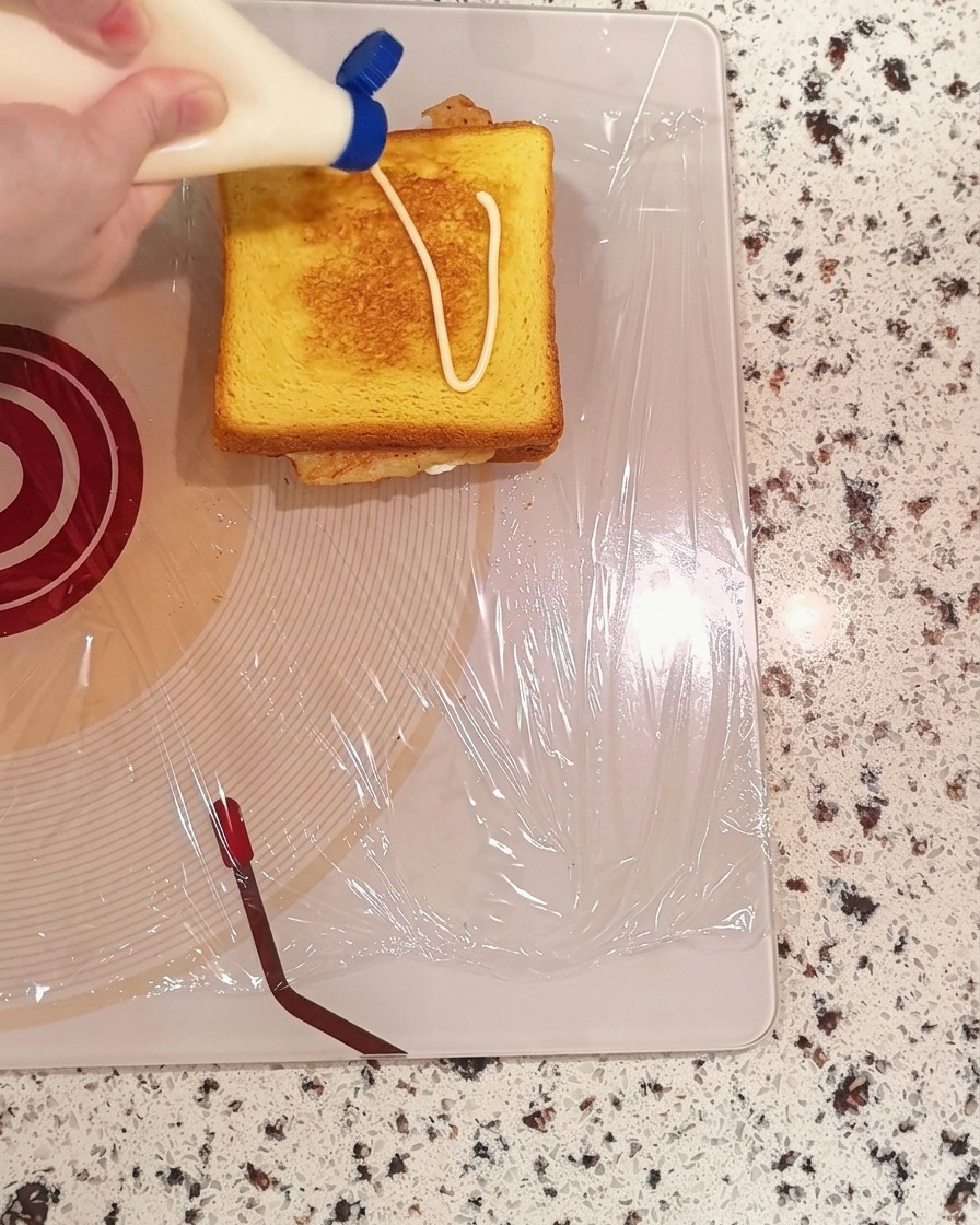 Mayonesa siendo exprimida en patrón de zigzag sobre una rebanada de pan tostado.