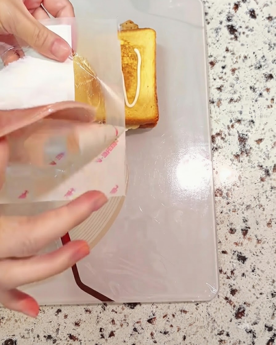 Una rebanada de jamón siendo colocada sobre los componentes del sándwich en ensamblaje.