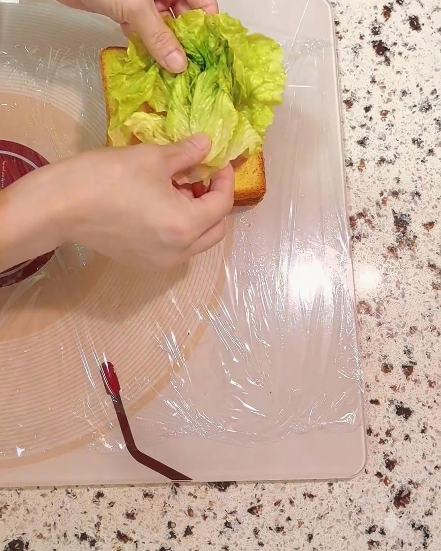Hojas de lechuga verde fresca siendo colocadas sobre las capas del sándwich.