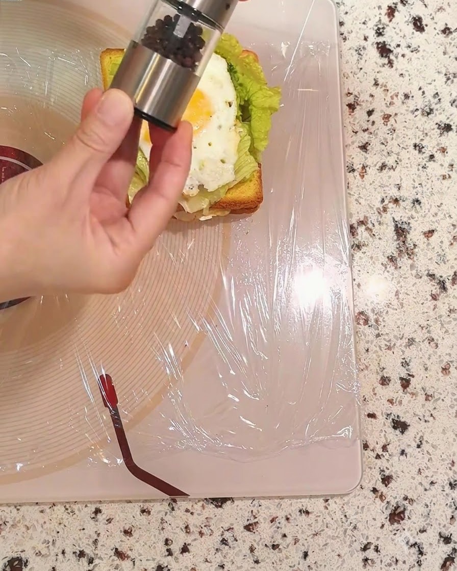 Una mano sosteniendo un molinillo de pimienta y espolvoreando pimienta negra sobre el huevo frito.