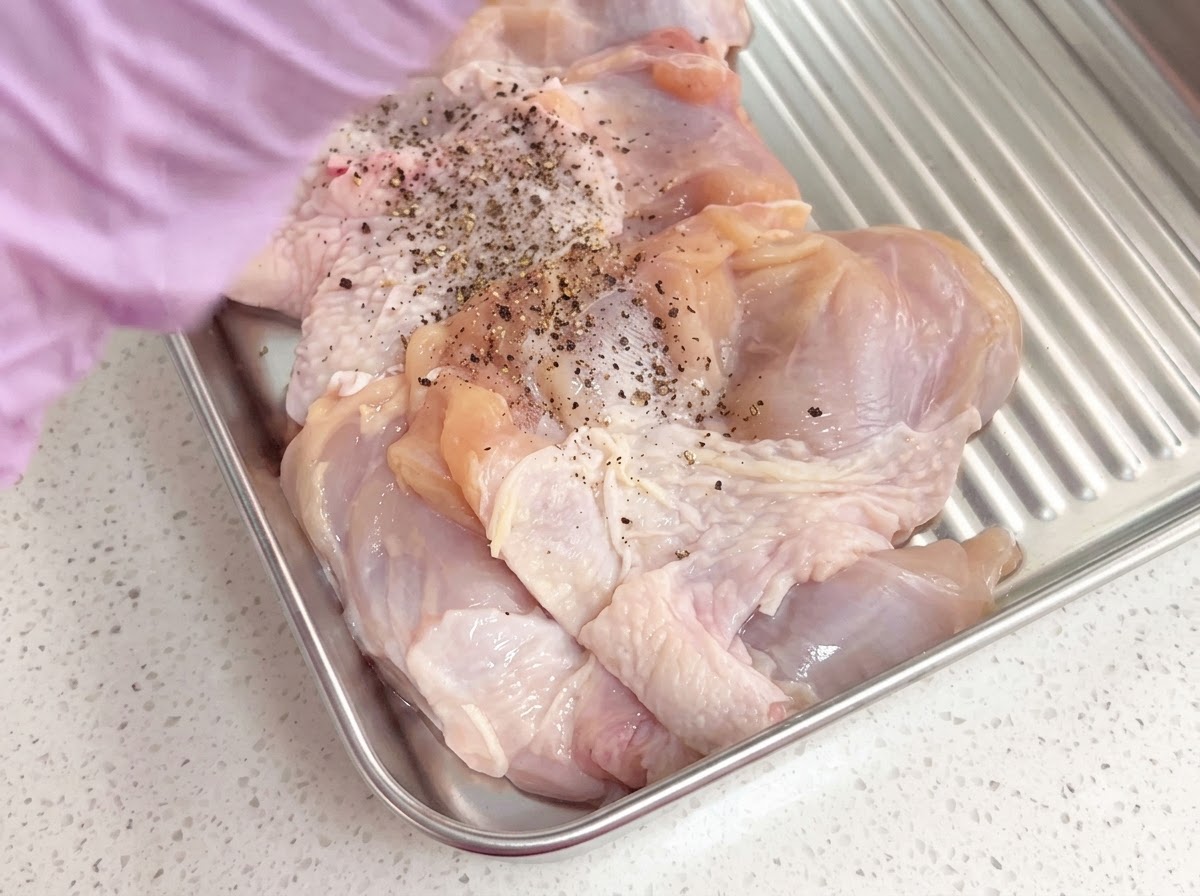Muslos de pollo deshuesados sazonados con pimienta negra recién molida dentro de una bandeja de metal.