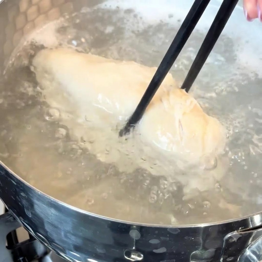 Una pechuga de pollo hirviendo en agua caliente dentro de una olla de cocina.