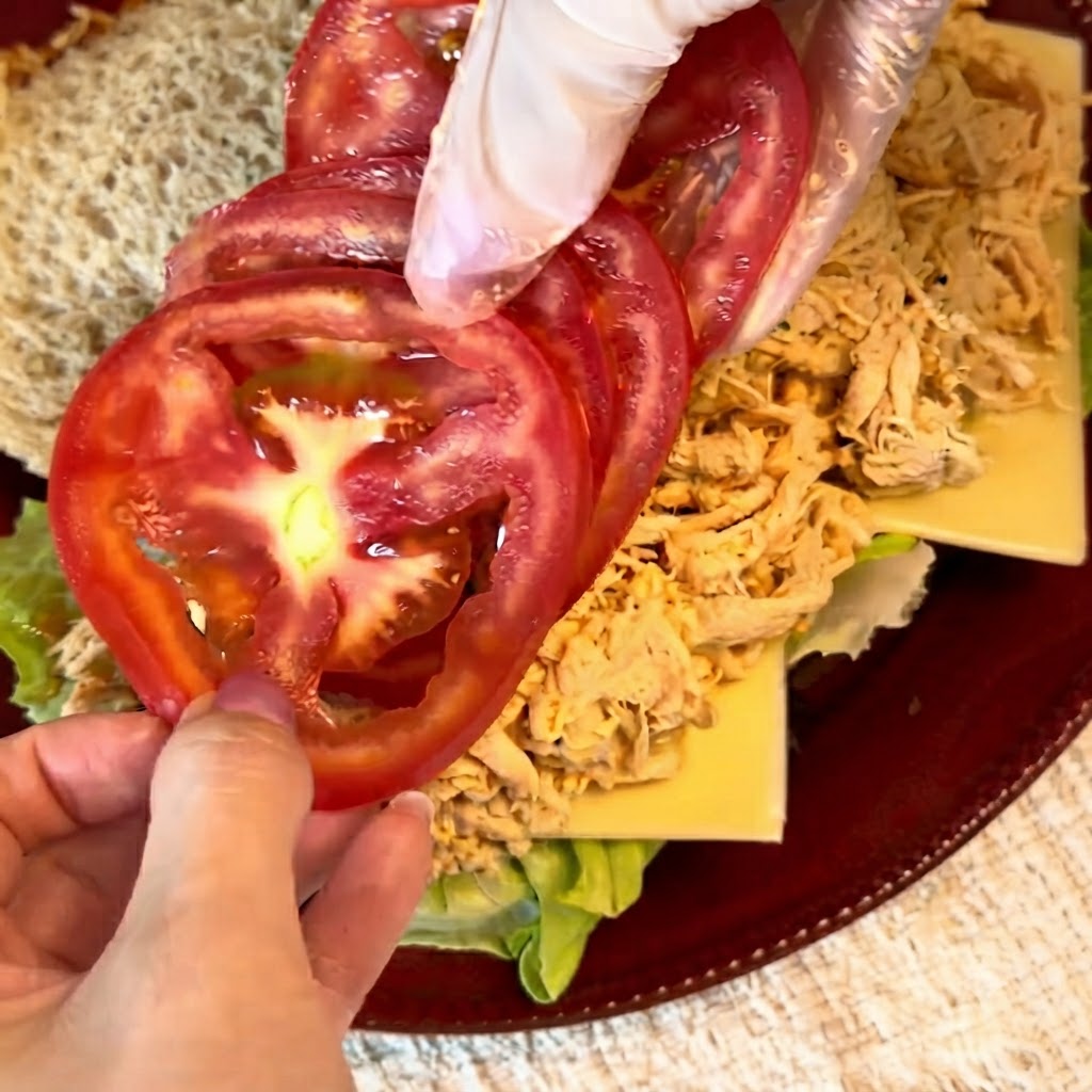 Rodajas de tomate rojo fresco siendo ordenadas cuidadosamente sobre el relleno de pollo desmenuzado.