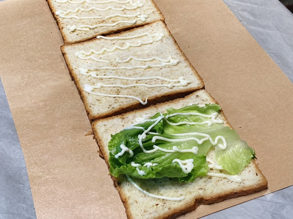 Rodajas de pepino verde fresco dispuestas en la segunda rebanada de pan tostado con un chorrito de mayonesa.