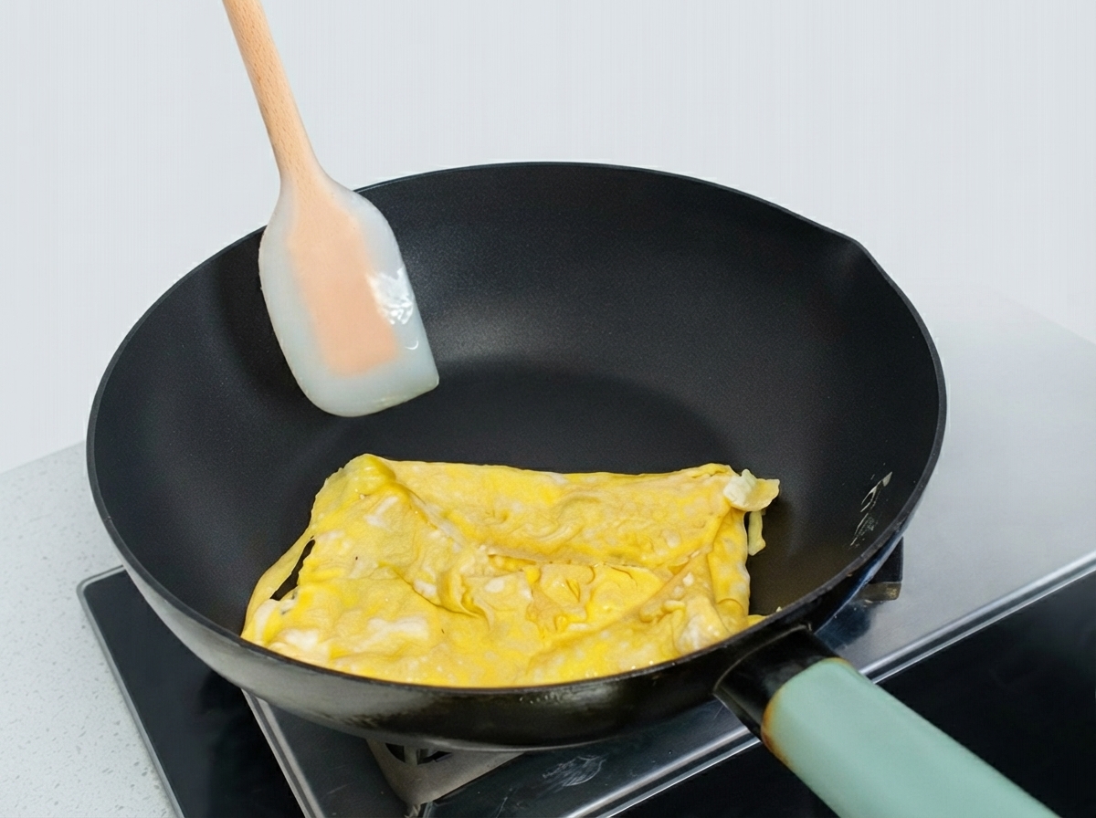 Tortilla de huevo parcialmente doblada en una sartén siendo moldeada con una espátula de silicona.