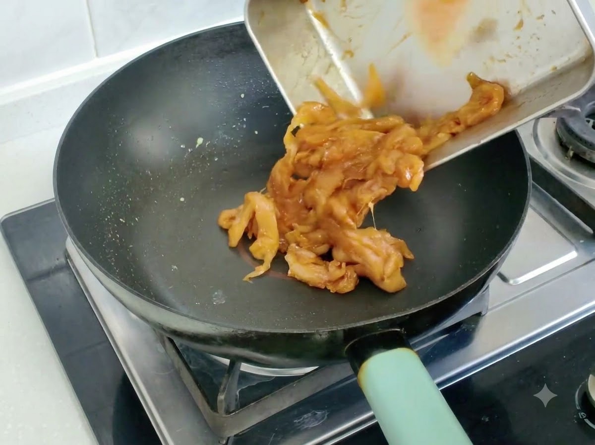 Trozos de pollo marinado siendo vaciados y salteados en una sartén.