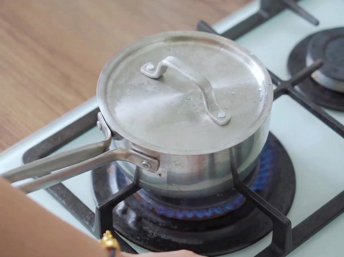 Una olla tapada en una estufa encendida con vapor escapando, cocinando la pechuga de pollo.