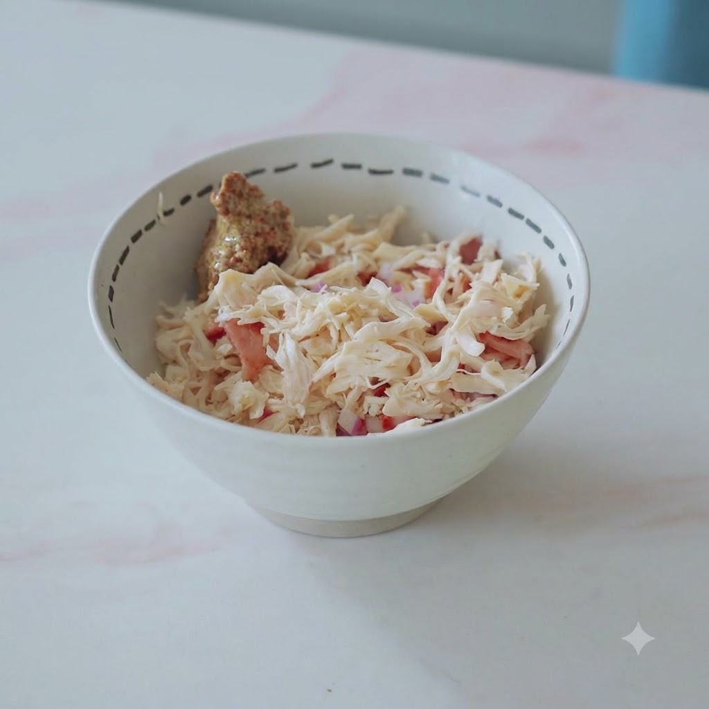 Un tazón lleno de pollo desmenuzado, tocino, cebollas y una cucharada de mostaza listo para ser mezclado.