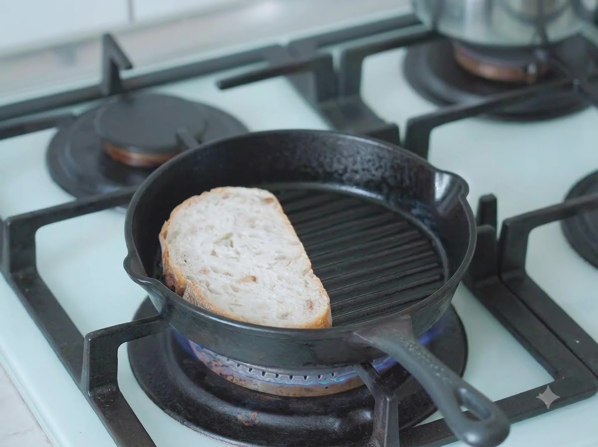 Una rebanada de pan de masa madre tostándose en una sartén grill de hierro fundido en la estufa.