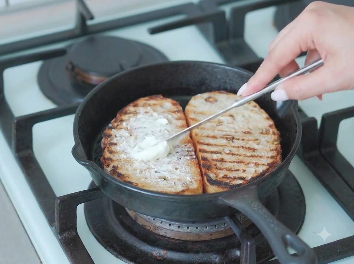 Hojas de rúcula verde fresca siendo colocadas sobre la capa de queso crema en el pan de masa madre.