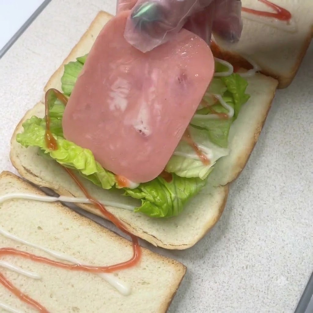 Una rebanada de jamón colocada sobre una capa de lechuga en un pan de sándwich con aderezos.