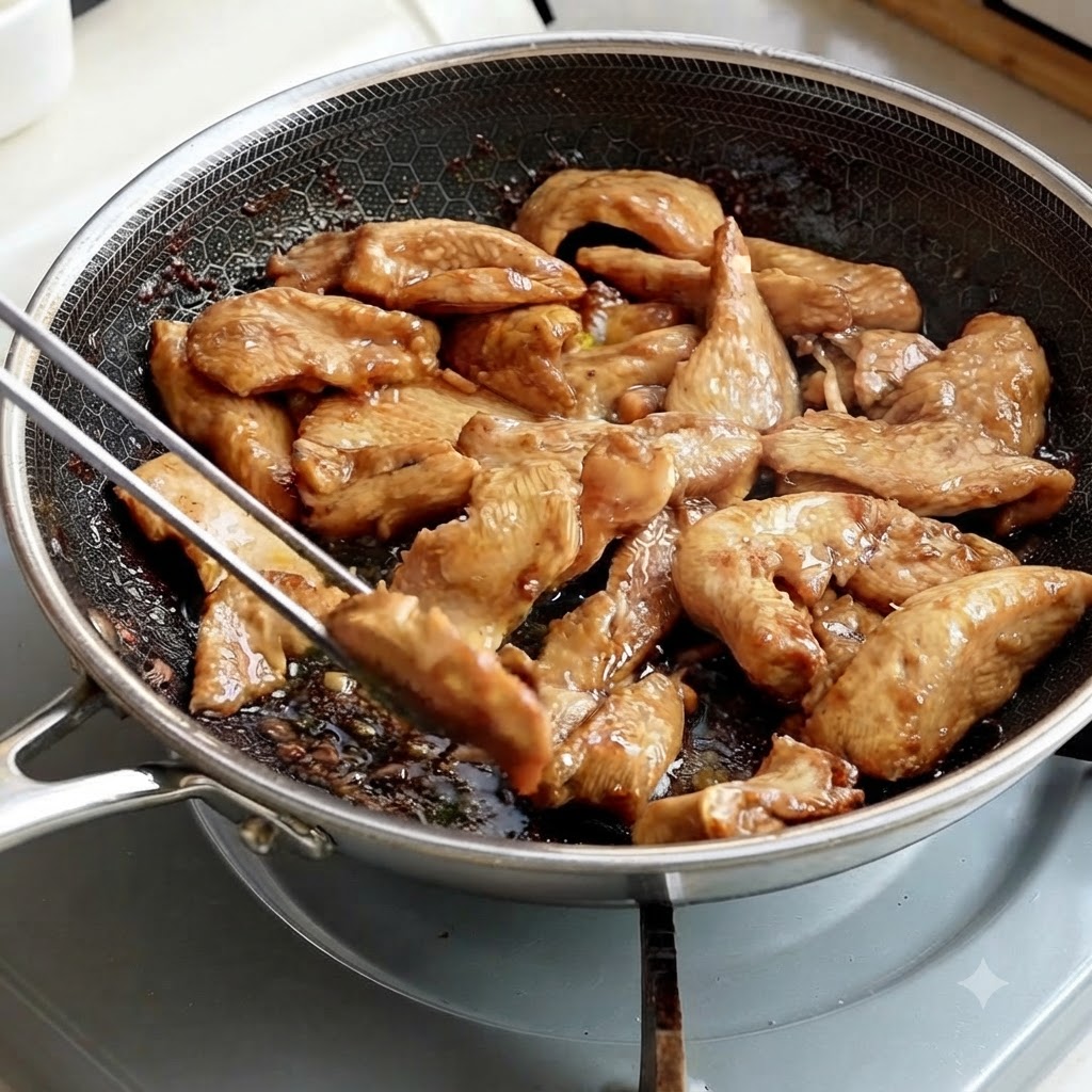 Pinzas metálicas levantando tiras de pollo cocinadas de una sartén.