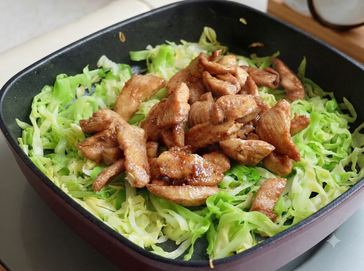 Tiras de pechuga de pollo cocinadas colocadas encima de la col rallada en la sartén, divididas en dos secciones.