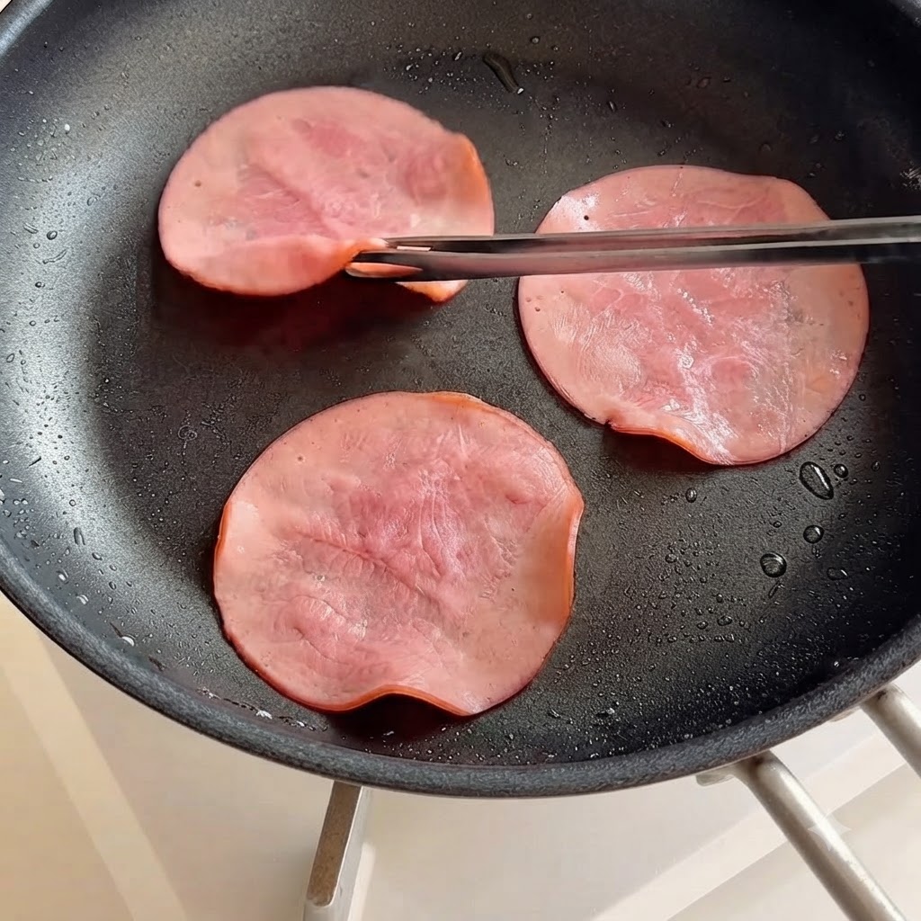 Rodajas de jamón siendo volteadas en una sartén usando palillos.