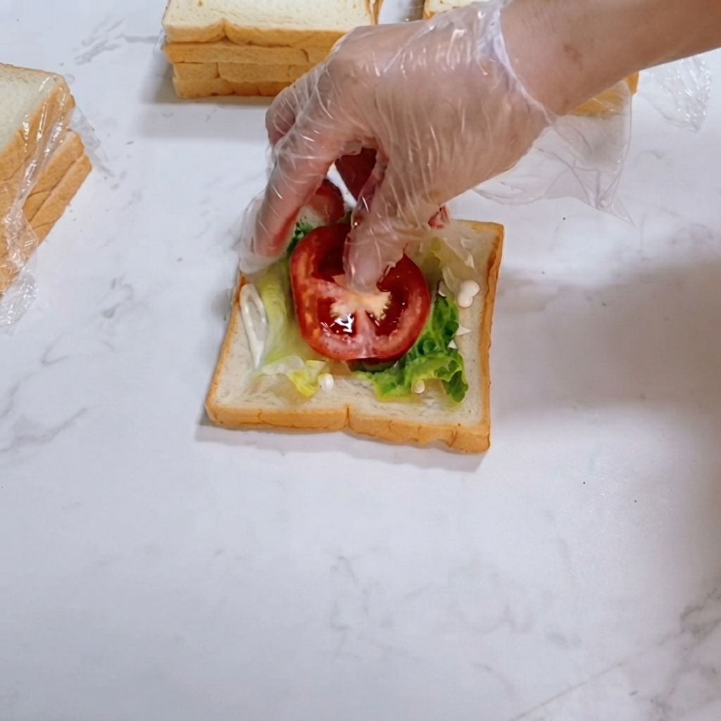 Rodajas de tomate rojo fresco colocadas cuidadosamente sobre la lechuga verde en la rebanada de pan.