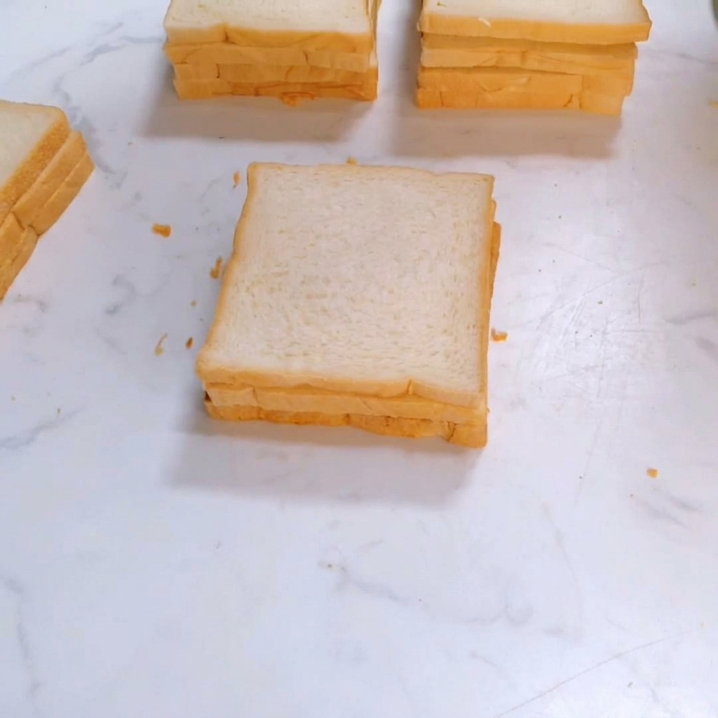 Una tercera rebanada de pan de molde cuadrado colocándose encima de la pila del sándwich.
